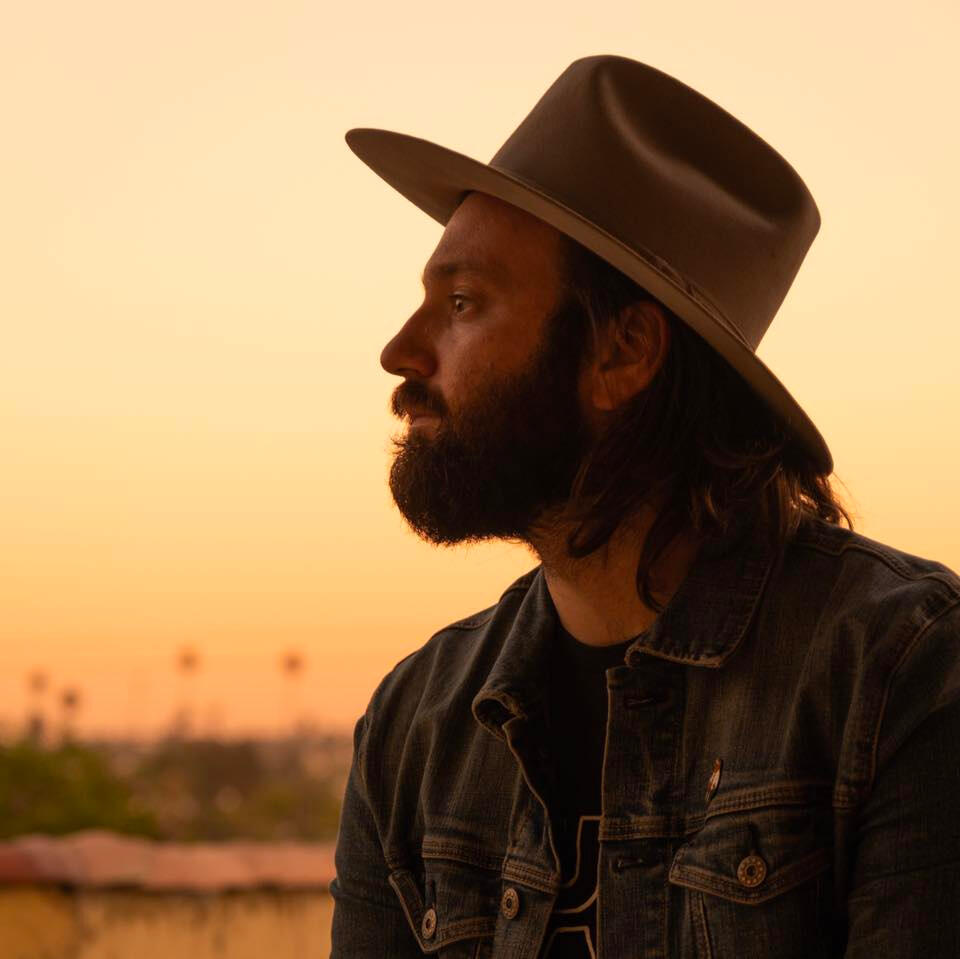 Profile of Nick Costa in a cowboy hat and jean jacket as sun sets.